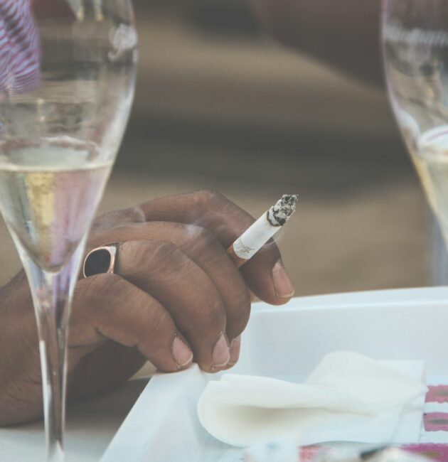 a person sitting at a table with wine glasses and a cigarette