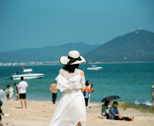 a woman in a white dress and hat standing on a beach