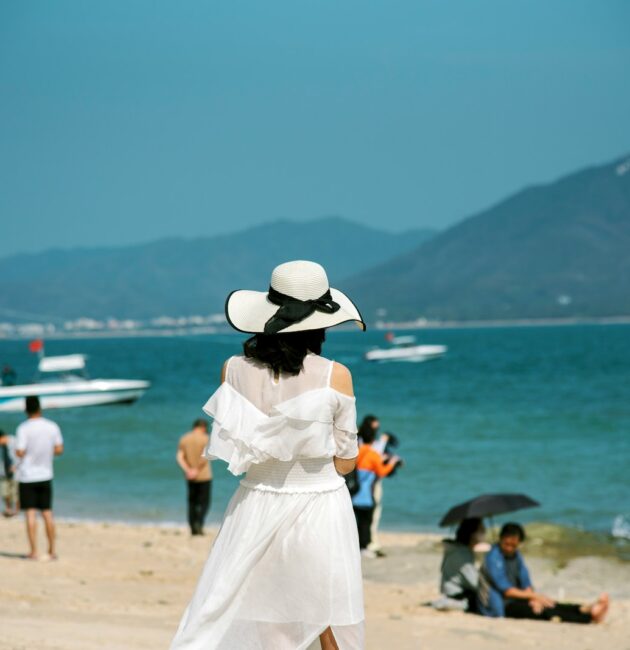 a woman in a white dress and hat standing on a beach